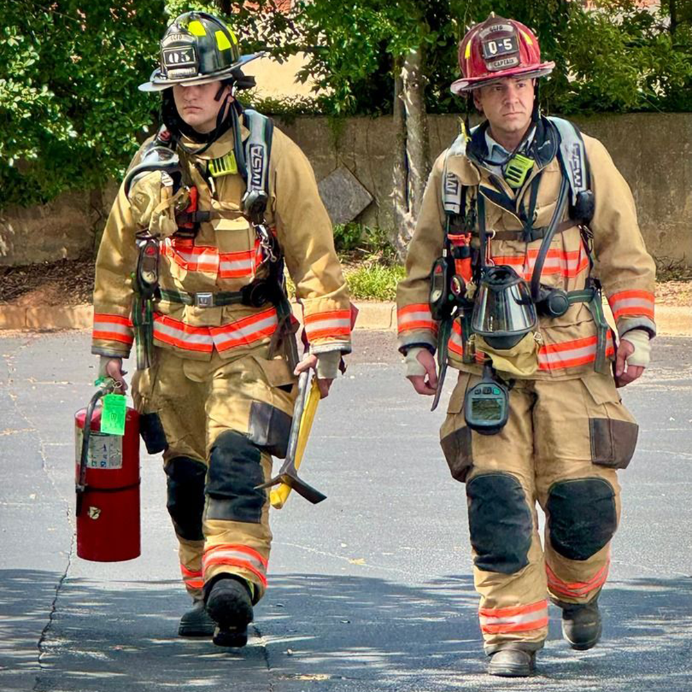 Two firefighters in full gear walking from a scene